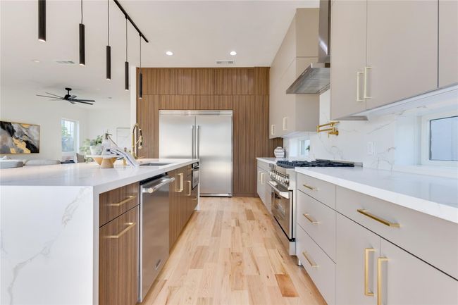 Kitchen featuring tasteful backsplash, premium appliances, light stone counters, wall chimney exhaust hood, and light wood-type flooring | Image 11