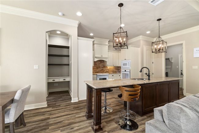 The spacious island includes an extended breakfast bar, illuminated by two stunning pendant lights overhead. Just off the kitchen, a cozy niche features open shelving and a convenient desk area. | Image 12