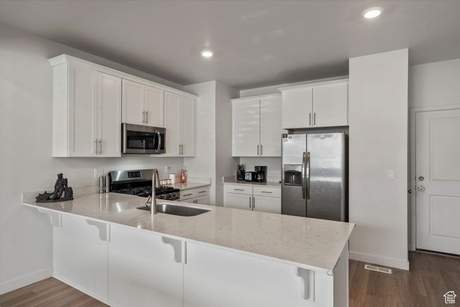 Kitchen featuring dark wood finished floors, a peninsula, appliances with stainless steel finishes, light stone countertops, and a kitchen bar | Image 7