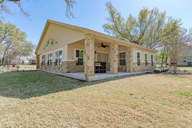 Rear view of property featuring a ceiling fan, stone siding, a lawn, and a patio | Image 40