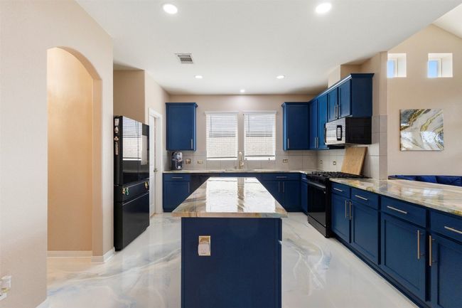 Kitchen featuring black appliances, blue cabinets, backsplash, and recessed lighting | Image 6