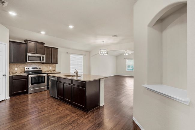 Kitchen with appliances with stainless steel finishes, dark wood-style flooring, decorative backsplash, dark brown cabinets, and light stone countertops | Image 9