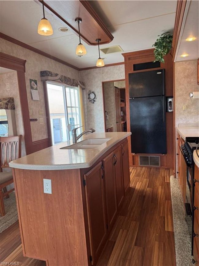 Kitchen featuring an island with sink, hanging light fixtures, sink, ornamental molding, and fridge | Image 31