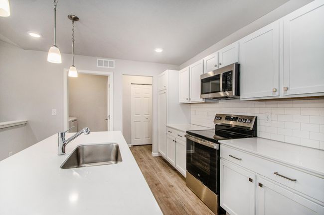 Bright, white kitchen cabinetry is accented by white quartz counters and tile backsplash. The kitchen island provides prep and sitting space and is accented by pendant lighting above. Stainless steel appliances are included! | Image 4