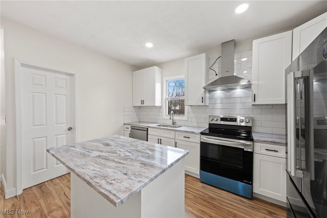 Kitchen featuring appliances with stainless steel finishes, wall chimney exhaust hood, sink, white cabinets, and a kitchen island | Image 11