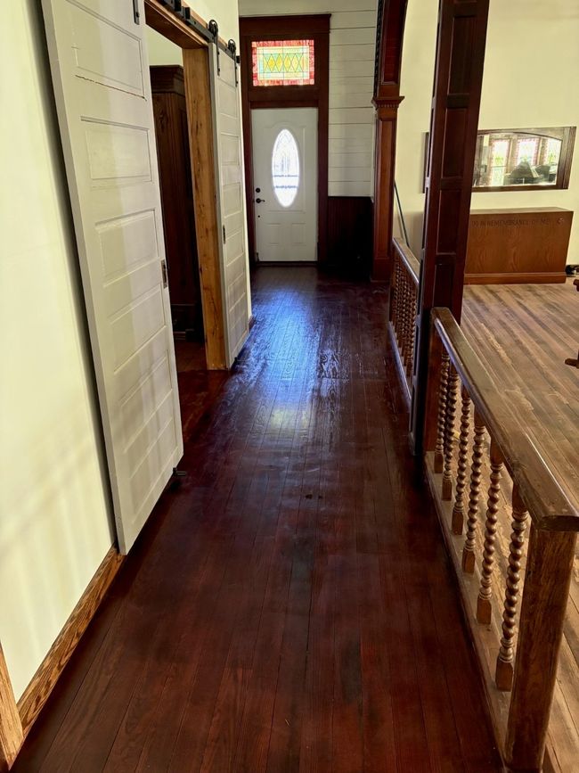 Corridor with dark wood-type flooring, wooden walls, a barn door, and a wainscoted wall | Image 9