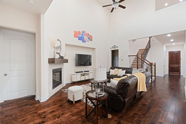 Living area with a glass covered fireplace, a ceiling fan, stairs, hardwood / wood-style floors, and a towering ceiling | Image 11