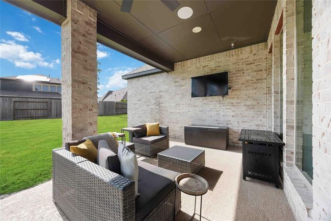 This photo showcases a covered patio with stylish wicker furniture, a mounted TV, and a view of a spacious grassy backyard, perfect for outdoor relaxation and entertainment. | Image 35