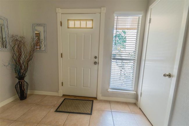 This photo shows a welcoming entryway with a white front door featuring a window and light tiled flooring, creating a cozy and inviting atmosphere. | Image 5