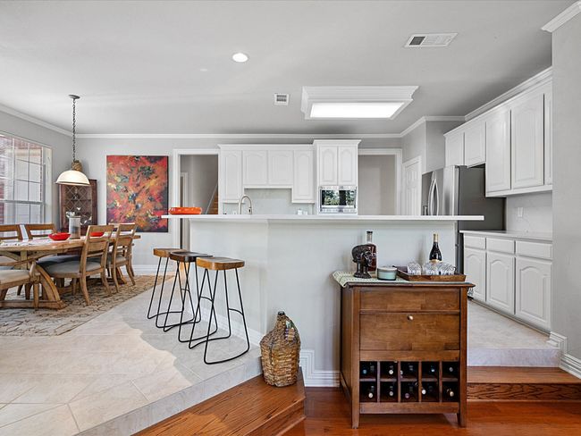 Kitchen featuring white cabinets, a breakfast bar, ornamental molding, pendant lighting, and natural stone countertops. Dining area on left. | Image 10