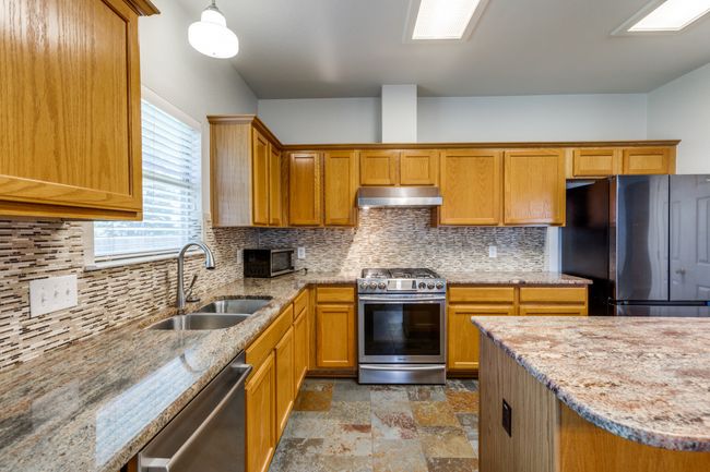 Kitchen featuring appliances with stainless steel finishes, under cabinet range hood, stone finish flooring, tasteful backsplash, and light stone countertops | Image 16
