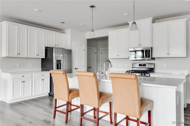 Kitchen with stainless steel appliances, light wood-style floors, a kitchen bar, and a center island with sink | Image 11