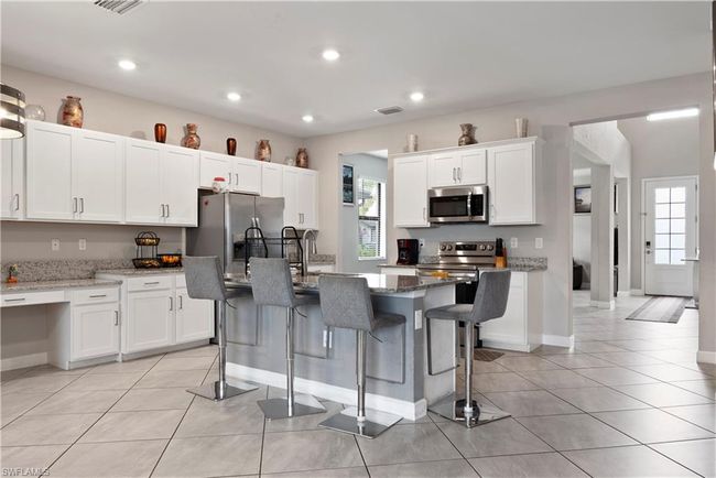 Kitchen featuring white cabinetry, light stone countertops, stainless steel appliances, light tile patterned floors, and visible vents | Image 12