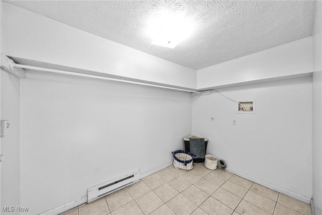 Clothes washing area featuring light tile patterned flooring, hookup for a washing machine, a textured ceiling, and a baseboard heating unit | Image 25