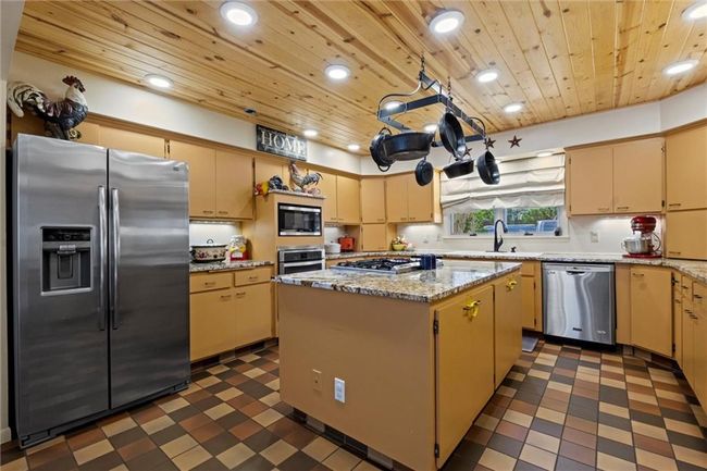 Kitchen featuring stainless steel appliances, wooden ceiling, recessed lighting, a center island, and dark flooring | Image 6
