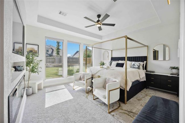 This spacious primary, bedroom features a stylish canopy bed, large windows for natural light, modern furnishings, and a cozy sitting area. Neutral tones and a ceiling fan add to its inviting ambiance. | Image 22