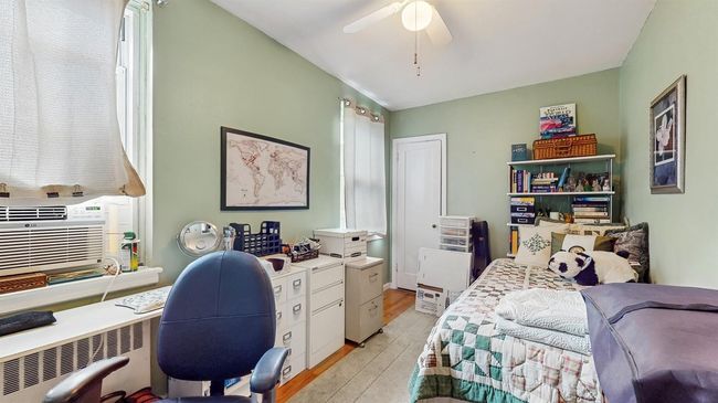 Bedroom featuring light wood finished floors, a desk, radiator heating unit, ceiling fan, and cooling unit | Image 14