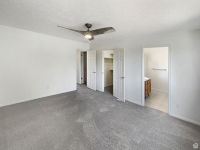 Unfurnished bedroom featuring a spacious closet, ceiling fan, ensuite bathroom, and a textured ceiling | Image 3