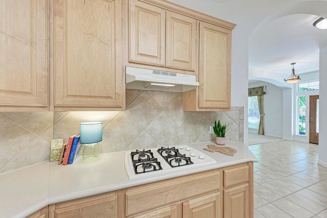 Kitchen featuring arched walkways, under cabinet range hood, white gas stovetop, and light brown cabinetry | Image 20