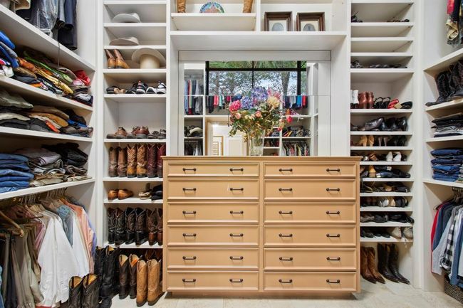 The primary closet was intentionally designed for optimal storage capacity and organization. Windows provide natural light in a traditionally dark space. Clothing, shoes and accessories have designated spaces within the custom shelves, drawers and rods. Top closet pull down rods ensure vertical space is not wasted. | Image 22