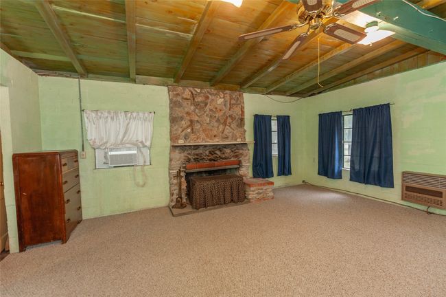 Unfurnished living room with beamed ceiling, a ceiling fan, carpet floors, wood ceiling, and heating unit | Image 16