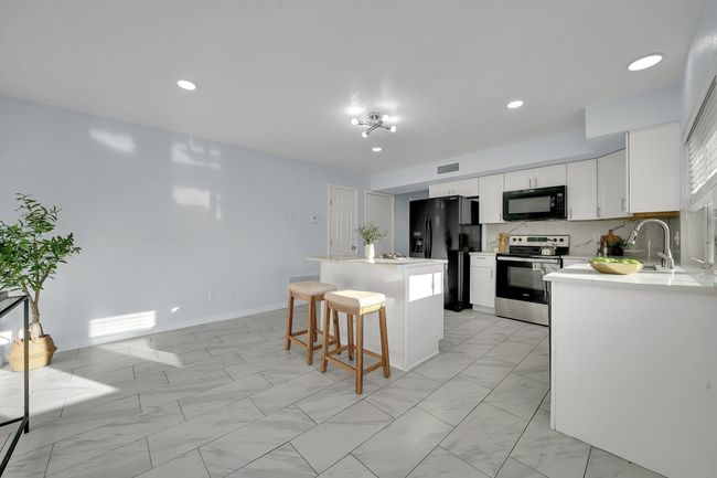 Kitchen featuring black appliances, light marble finish floors, a kitchen island, a breakfast bar area, and light countertops | Image 27