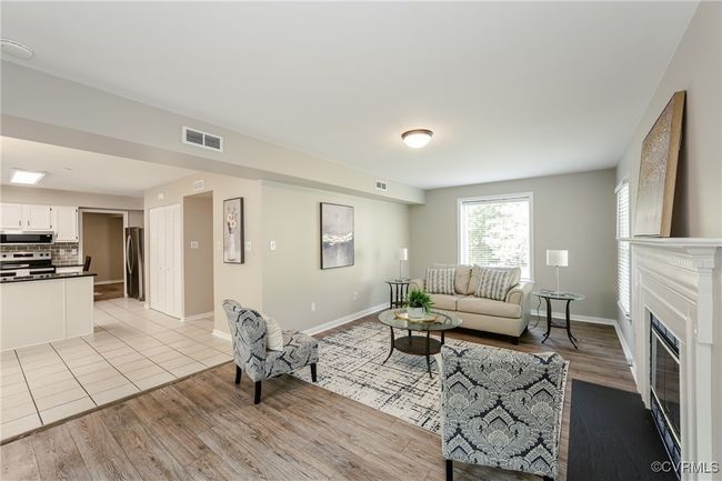 Living room featuring a fireplace with flush hearth, baseboards, light wood-style flooring, and visible vents | Image 23