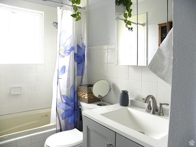 Bathroom with shower / bath combo, decorative backsplash, toilet, tile walls, and vanity | Image 22