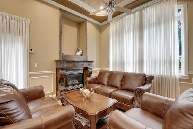 Living room featuring a decorative wall, a wainscoted wall, ceiling fan, a glass covered fireplace, and crown molding | Image 5