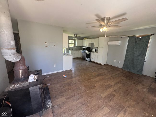 unfurnished living room with dark wood-type flooring, ceiling fan, an AC wall unit, and a wood stove | Image 7