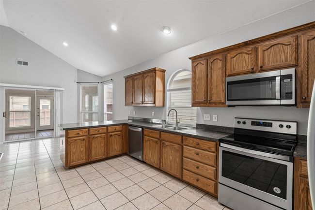 Kitchen featuring appliances with stainless steel finishes, a peninsula, dark countertops, light tile patterned floors, and recessed lighting | Image 22