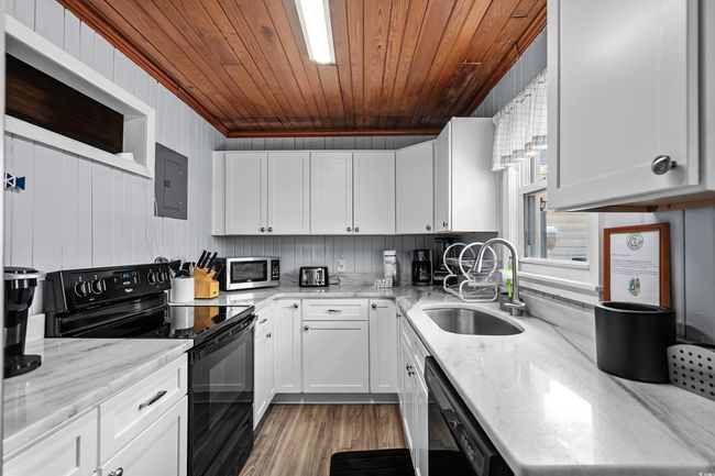 Kitchen with black appliances, a sink, electric panel, wood ceiling, and white cabinets | Image 8