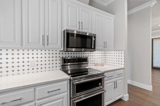Kitchen with crown molding, decorative backsplash, stainless steel appliances, light countertops, and white cabinetry | Image 10