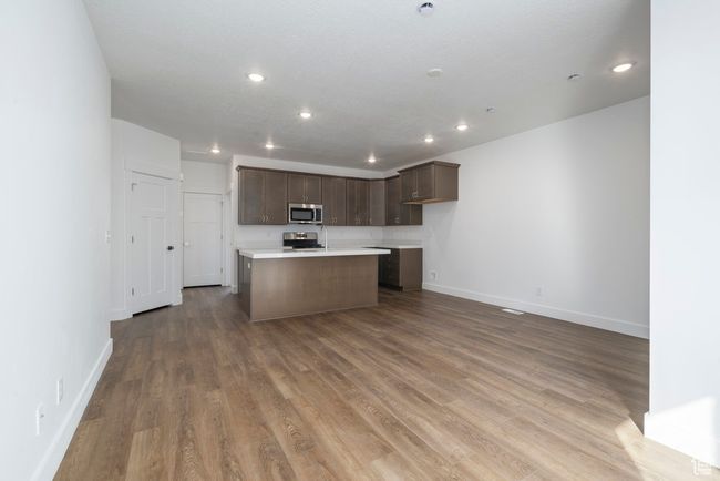 Kitchen with stainless steel appliances, wood finished floors, a kitchen island with sink, and light countertops | Image 10