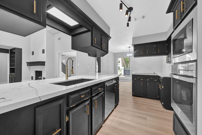 Sleek and stylish kitchen featuring bold black cabinetry with striking gold hardware, complemented by stunning white quartz countertops with dramatic veining. Brand-new stainless steel appliances, including oven, microwave, dishwasher, cooktop, and vent hood, offer both beauty and function. A modern pull-down faucet and statement lighting complete this sophisticated culinary space. | Image 14