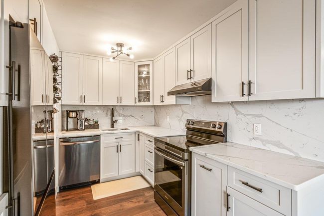 Kitchen featuring appliances with stainless steel finishes, under cabinet range hood, dark wood-style flooring, glass insert cabinets, and white cabinets | Image 15