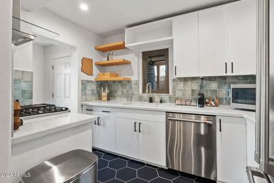 The kitchen features sleek stainless steel appliances, including a large refrigerator, a built-in oven, and a gas stove with a modern range hood. The cabinetry is a bright white, offering a clean and contemporary look that contrasts beautifully. | Image 3