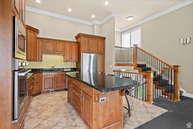 Kitchen featuring stainless steel appliances, crown molding, brown cabinetry, a center island, and a breakfast bar area | Image 15
