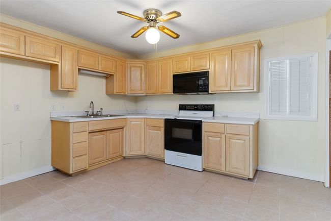 Kitchen featuring light countertops, light brown cabinetry, a sink, black microwave, and range with electric cooktop | Image 11