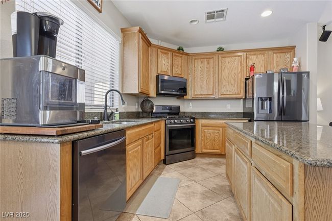 Kitchen featuring appliances with stainless steel finishes, a sink, dark stone countertops, light tile patterned flooring, and recessed lighting | Image 25