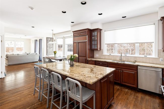 Kitchen with paneled built in refrigerator, stainless steel dishwasher and stove, center island with seating and glass insert cabinets | Image 12
