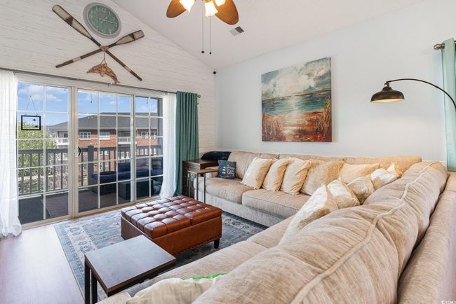 Living room with a ceiling fan, lofted ceiling, wood finished floors, and visible vents | Image 4