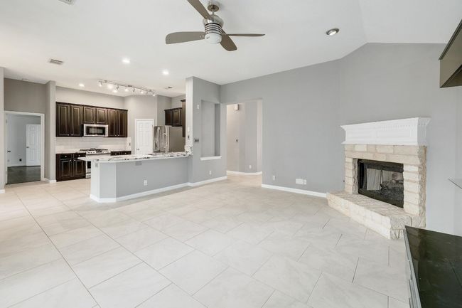 Unfurnished living room with light tile patterned floors, track lighting, a ceiling fan, a stone fireplace, and visible vents | Image 7