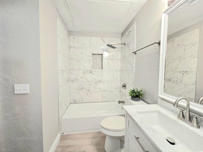 Bathroom with vanity, toilet, wood finished floors, bathtub / shower combination, and a textured wall | Image 12