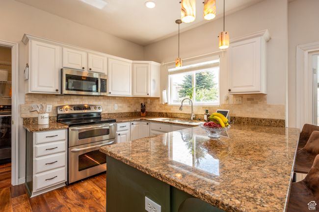 Kitchen featuring stainless steel appliances, a sink, a peninsula, white cabinetry, and stone countertops | Image 12