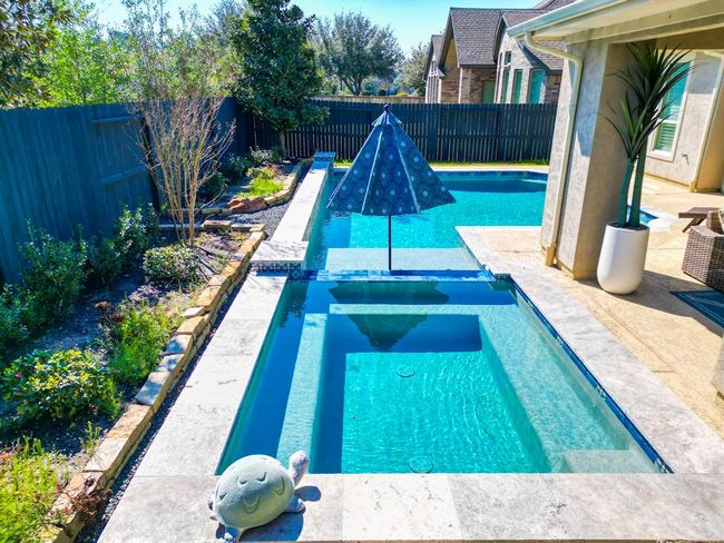 This photo showcases a backyard with a modern swimming pool featuring a connected spa. The area is surrounded by a landscaped garden with a privacy fence. A cozy patio with seating is visible, perfect for relaxation. | Image 44