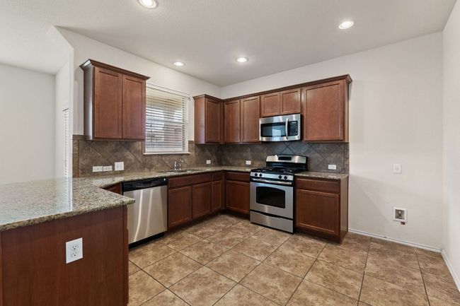 Kitchen featuring appliances with stainless steel finishes, backsplash, stone countertops, recessed lighting, and a peninsula | Image 7