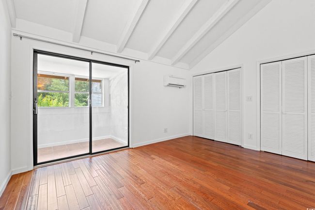 Unfurnished bedroom with a wall unit AC, wood-type flooring, and multiple closets | Image 12