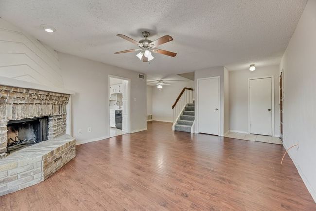 Unfurnished living room featuring a brick fireplace, a ceiling fan, stairs, a textured ceiling, and wood finished floors | Image 4