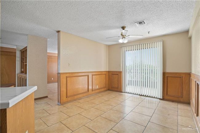 Spare room featuring a wainscoted wall, ceiling fan, a textured ceiling, light tile patterned flooring, and a decorative wall | Image 9